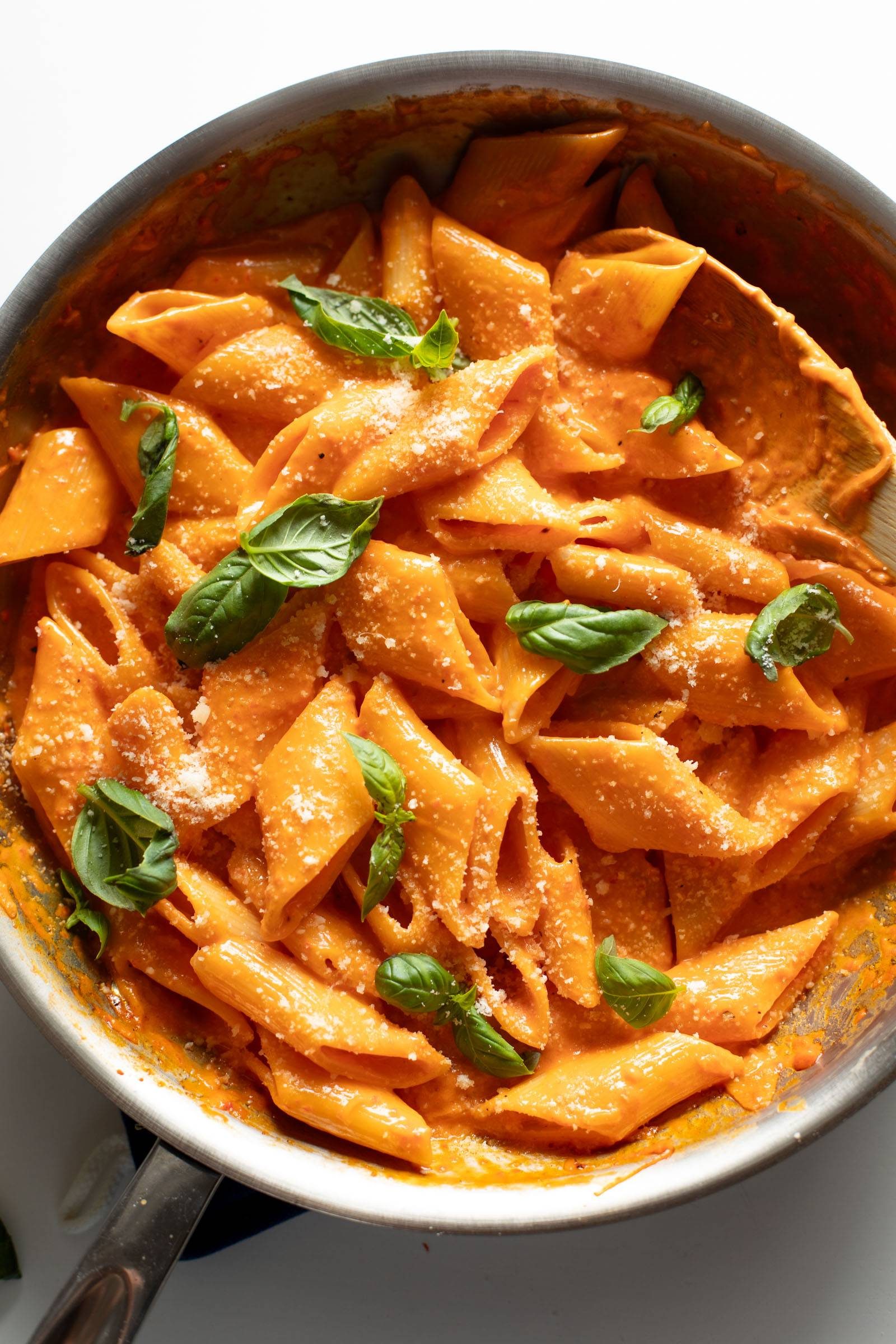 Roasted red pepper pasta in a pan topped with basil leaves and grated parmesan.